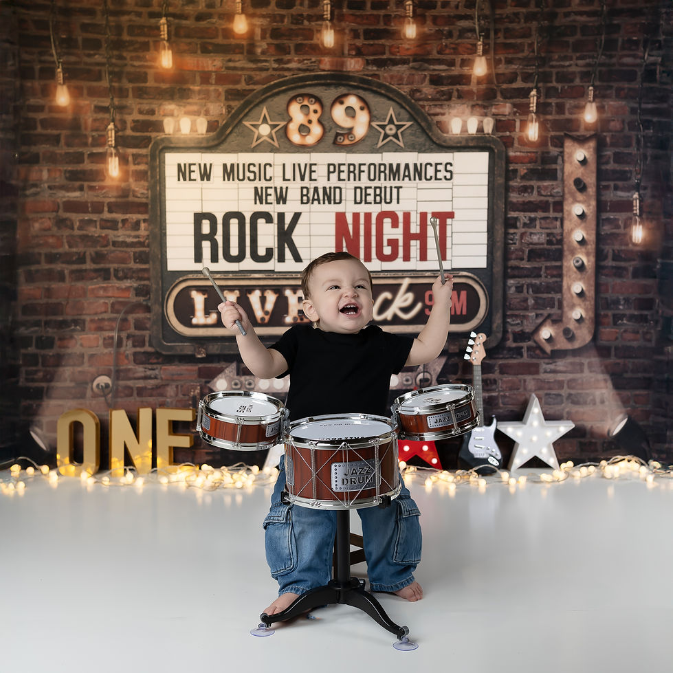Cake Smash Photography in the West Valley clost to Buckeye Arizona with a little boy playing the drums with a rockstar backdrop
