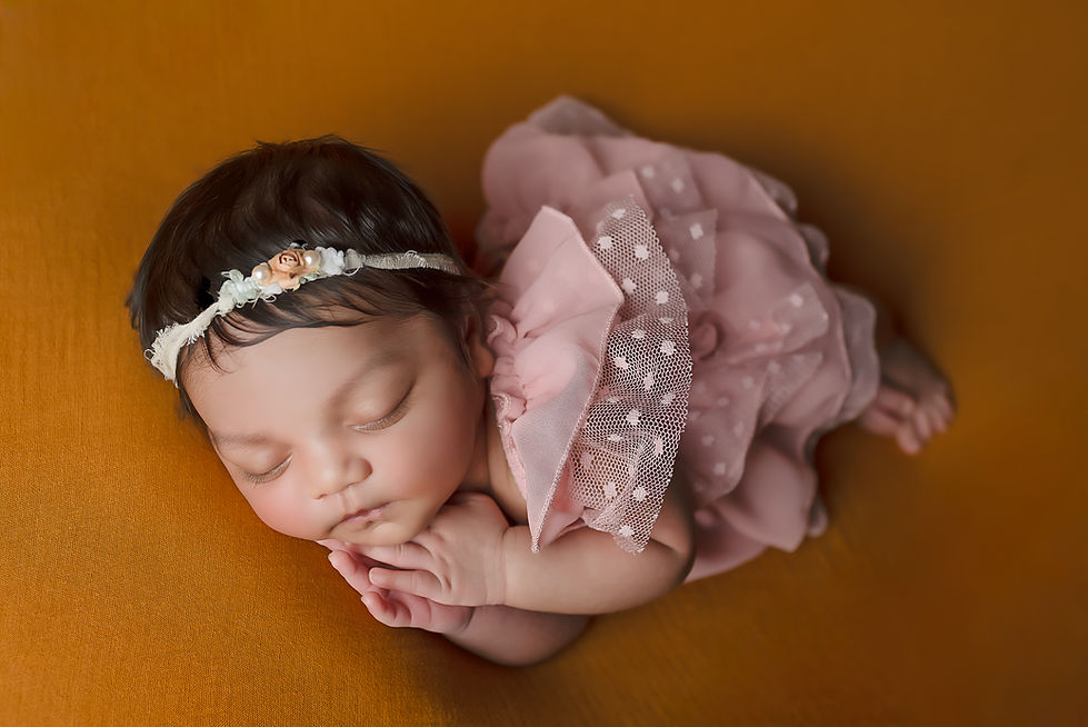 Newborn photography session in Buckeye AZ with a small baby laying on a cinnamon colored background wearing a dusty rose dress