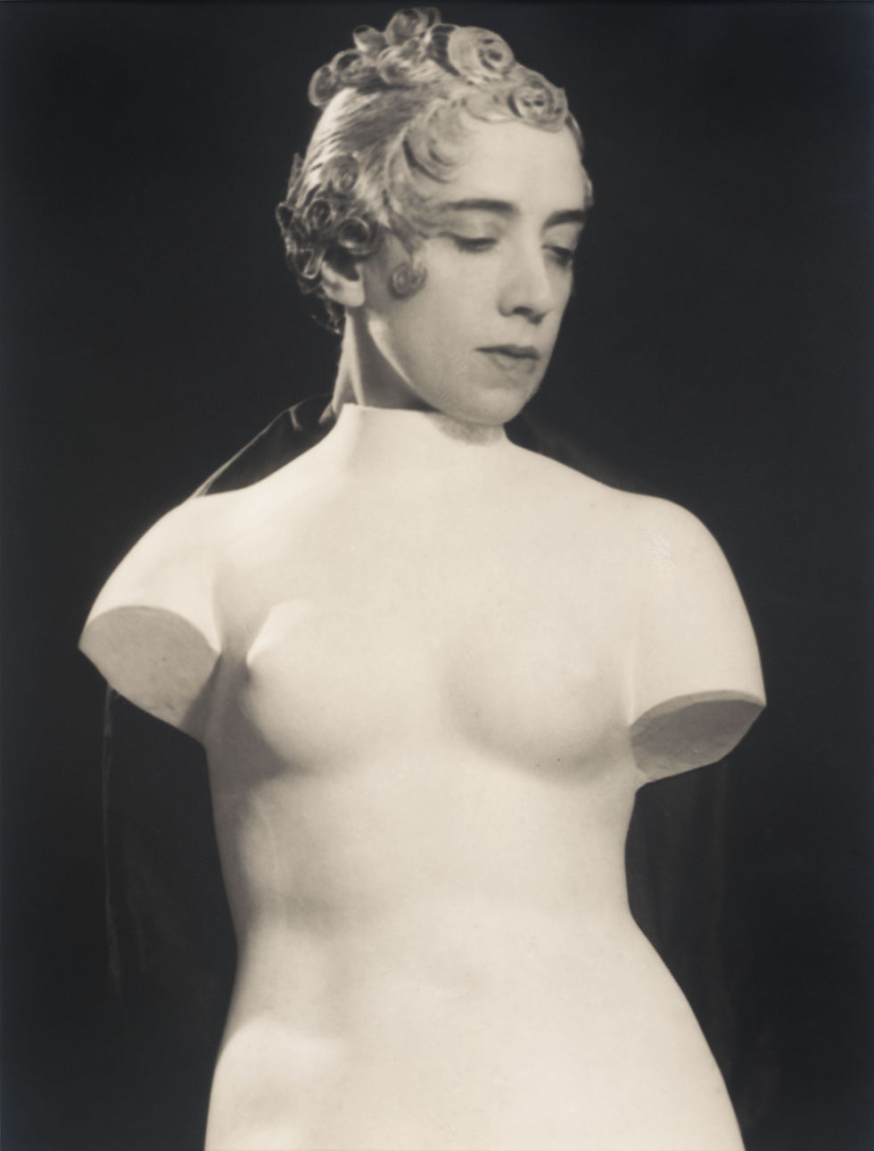 Surreal image of Schiaparelli posed as a marble bust, set against a black background, creating a melancholic and timeless mood created by Man Ray