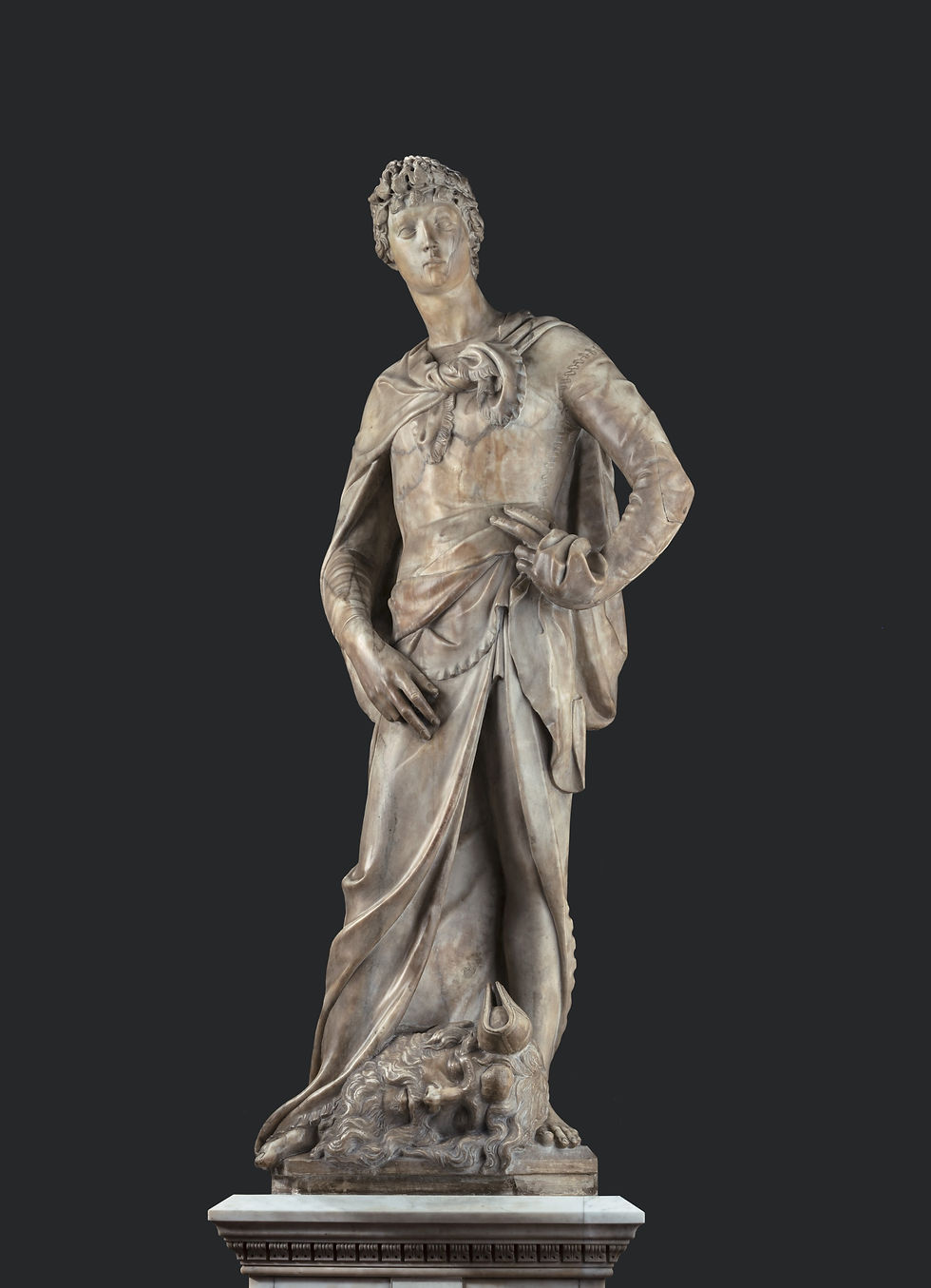 The marble statue of David by Donatello, standing on a plinth with a plain black background