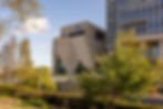 Modern building with "V&A" sign, tan geometric facade, foreground lush green trees, under clear blue sky, evokes calmness and creativity.