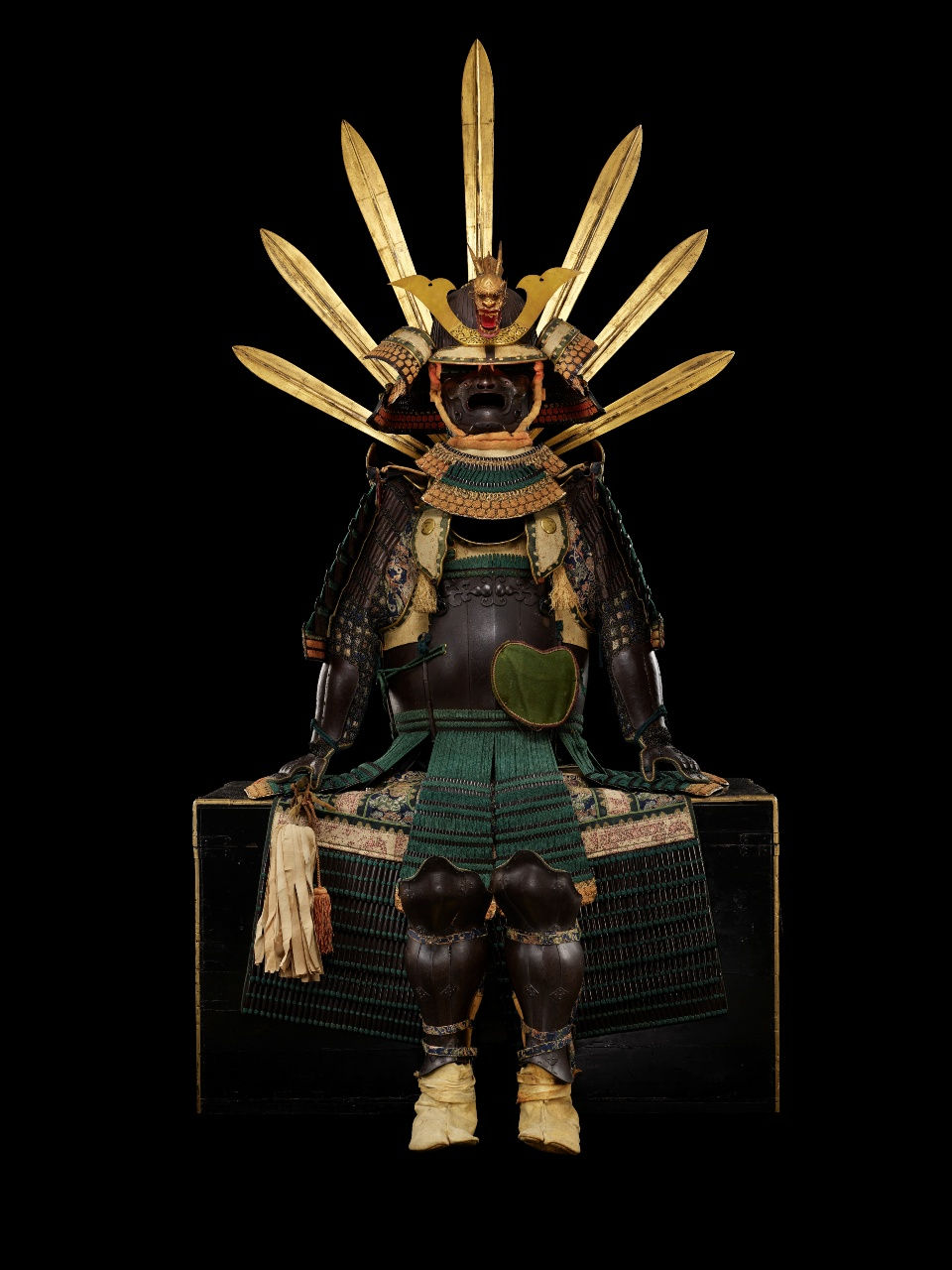 Ornate samurai armor with gold headpiece and fan-like blades sits against a black background. Rich green and brown details are visible.