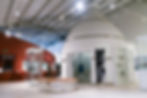 V&A Wedgwood Collection interior with modern displays of artifacts. A person blurred in motion. Red and white walls, high ceiling with spotlights. Quiet ambiance.