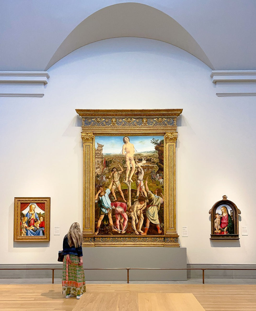A woman stands in a museum, admiring a large, colorful painting between two smaller ones on a white wall. Elegant decor, bright lighting.