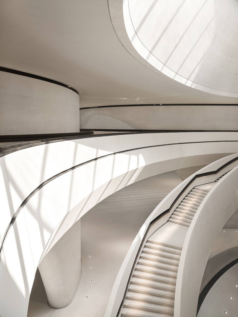 Inside the Zayed National Museum with its curved modern architecture with white staircases and flowing lines. Sunlight casts shadows on walls, creating an elegant, serene atmosphere.