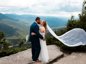 a couple in their wedding attire standing on stop of cannon mountain in the white mountains on their elopement day