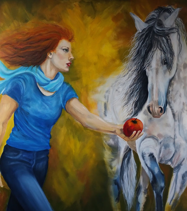 Red haired woman in blue with a blue scarf holds a red apple out to a grey horse