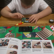 Boy building electronic circuit board, following detailed assembly instructions.