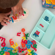 Little hands pressing colorful magnetic alphabet letters into dough.