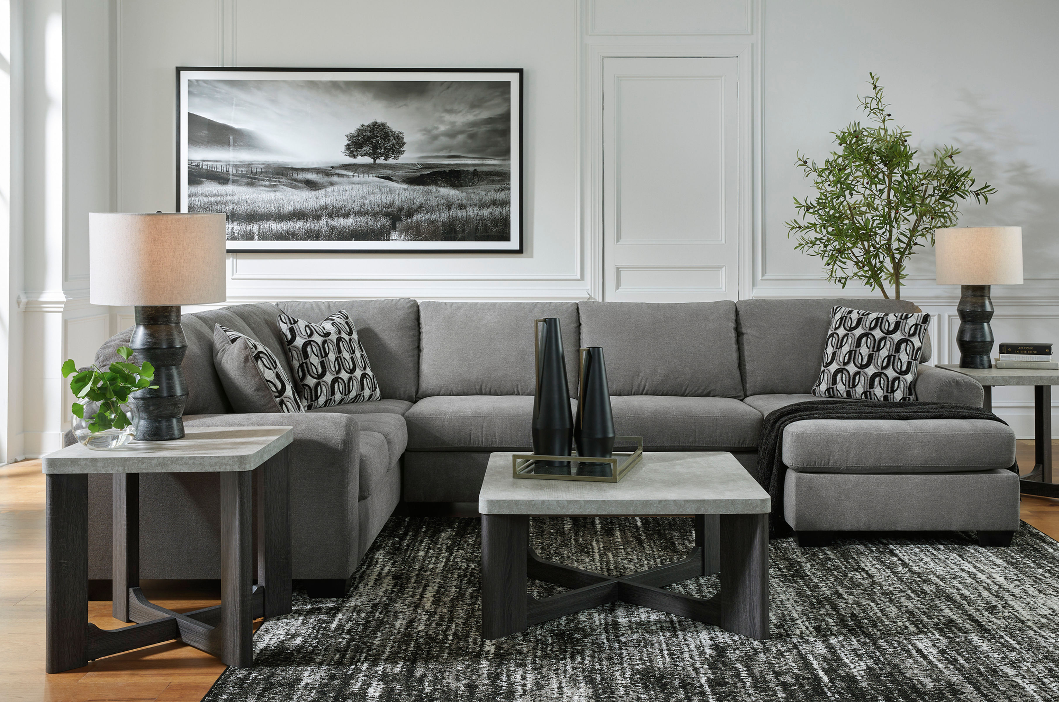 Gray sectional sofa with pillows, art, and two square tables.