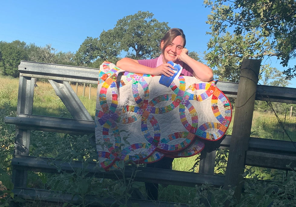 Elizabeth holding her blue ribbons posing with quilt