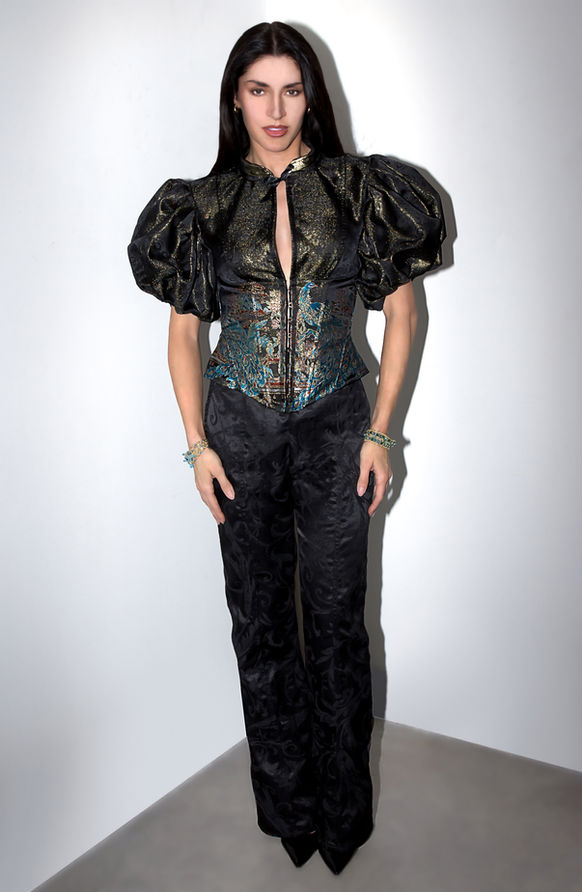 Model in a black brocade top with gold puff sleeves and a peacock corset detail.
