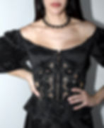 Model in a black off-shoulder top with puff sleeves and a sheer lace corset, paired with a textured black skirt.
