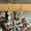 Thumbnail: A pair of gold dangle earrings with a large gold metal circle and two turquoise beads hanging in the middle and another smaller gold metal circle with one turquoise bead in the middle, hanging from it. The earrings are hanging from a gold metal bar with a plant in the background.