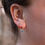 Thumbnail: An ear wearing a gold hoop earring with a light blue gem charm.
