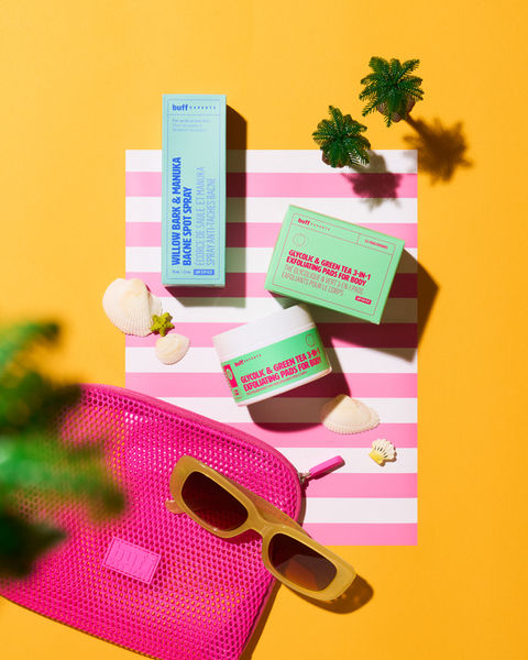 Flatlay product photography of Buff Experts bodycare products arranged on a bright orange background with miniature props