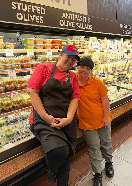Two happy employees pose near deli display with Stuffed Olives, Antipasti and salads.