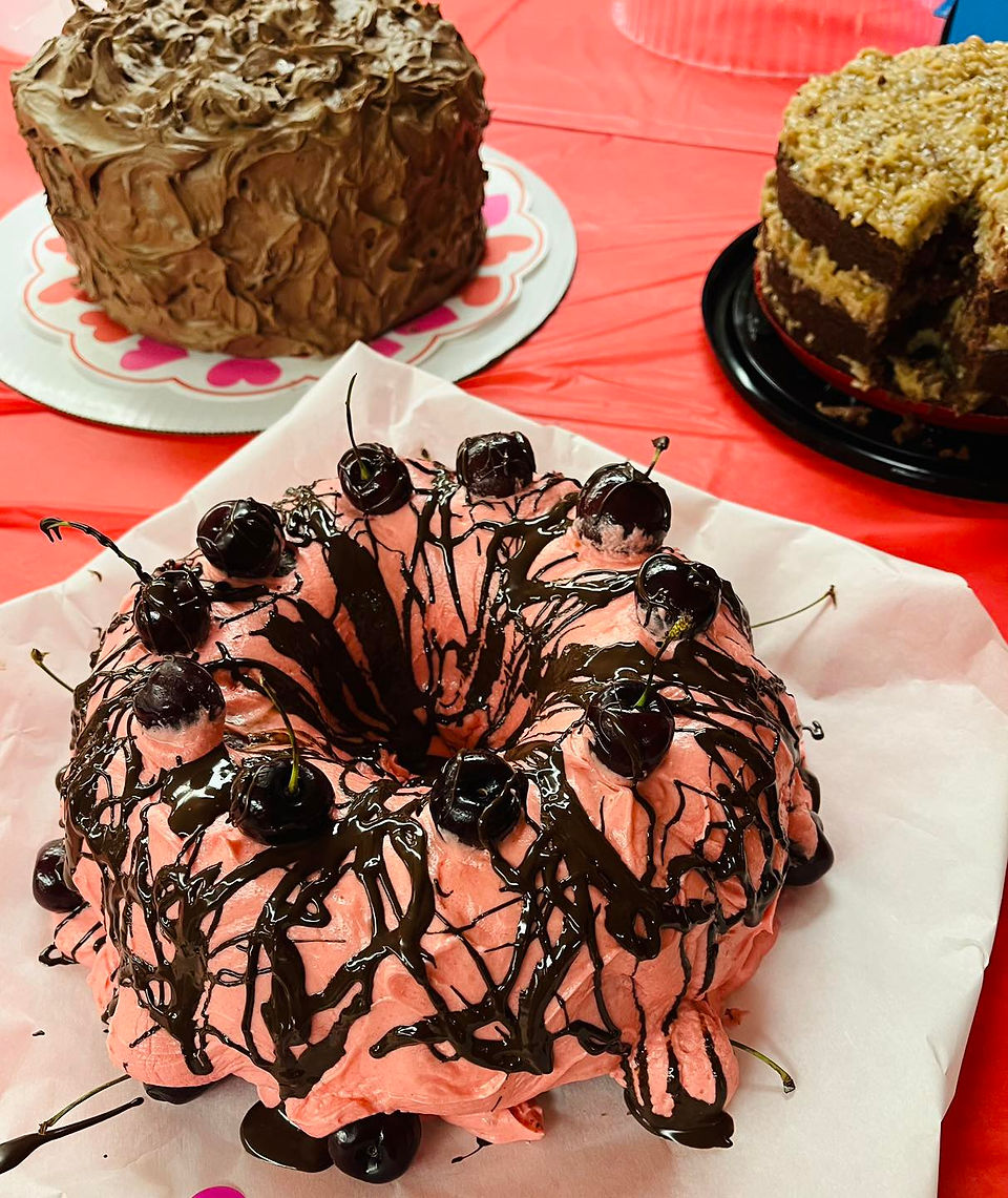 Three cakes. One in foreground has pink icing and chocolate covered cherries