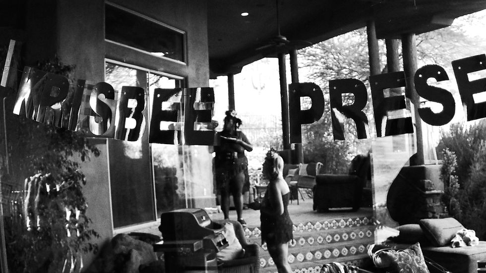 Kris and Bee on a patio enjoying their birthday party. In the foreground is a Kris Bee Presents sign.