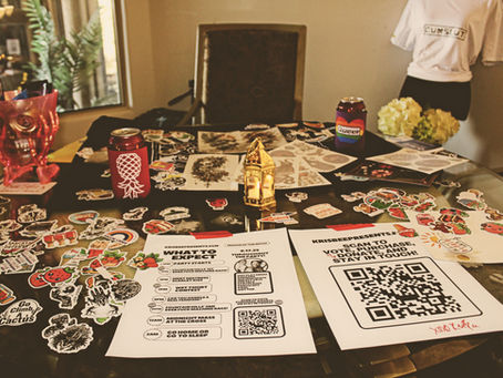 round table covered, nearly entirely by promotional stickers, a skull vase containing condoms, dental dams and lube, and 2 part flyers that are not readable.