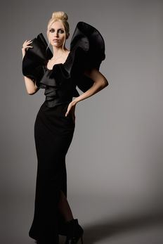 Fashion portrait on grey seamless Savage backdrop in a photography studio.  Model has platinum blonde hair and is wearing a black gown with flared sleeves.  