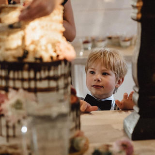 Kleiner Junge schaut neugierig auf Hochzeitstorte mit Schokoladenguss
