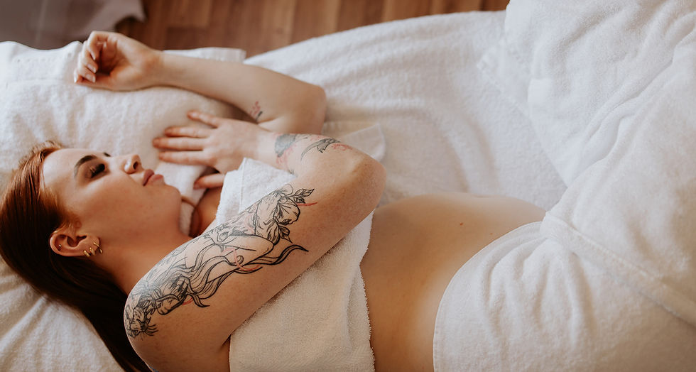 Person with tattoos relaxes on a white towel, eyes closed, in a peaceful setting. Wooden floor in background.