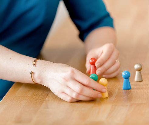 Frau mit blauem Kleid ordnet Spielfiguren auf einem Holztisch.