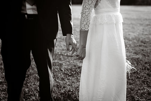 Mariés main dans la main dans un champ, la mariée tenant son bouquet, en noir et blanc