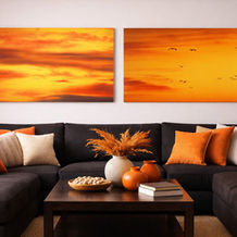 Two sunset paintings above a dark sectional sofa with orange pillows and decor