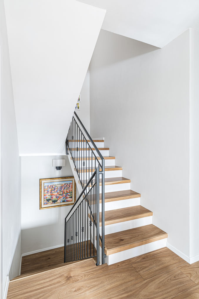 Wooden staircase with a metal railing and colorful artwork on the wall. Alyssa M. Interiors