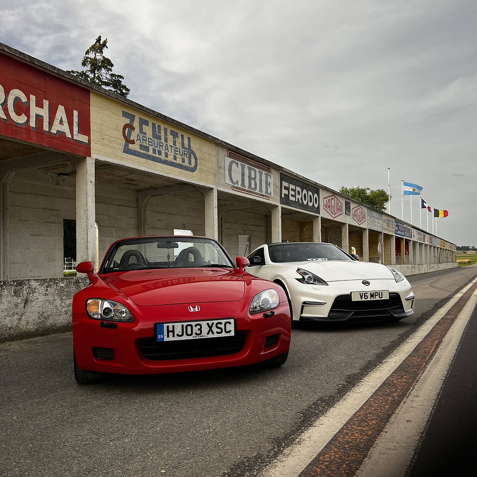 Red honda s2000 and white nissan 370z parked outside an abandoned race track