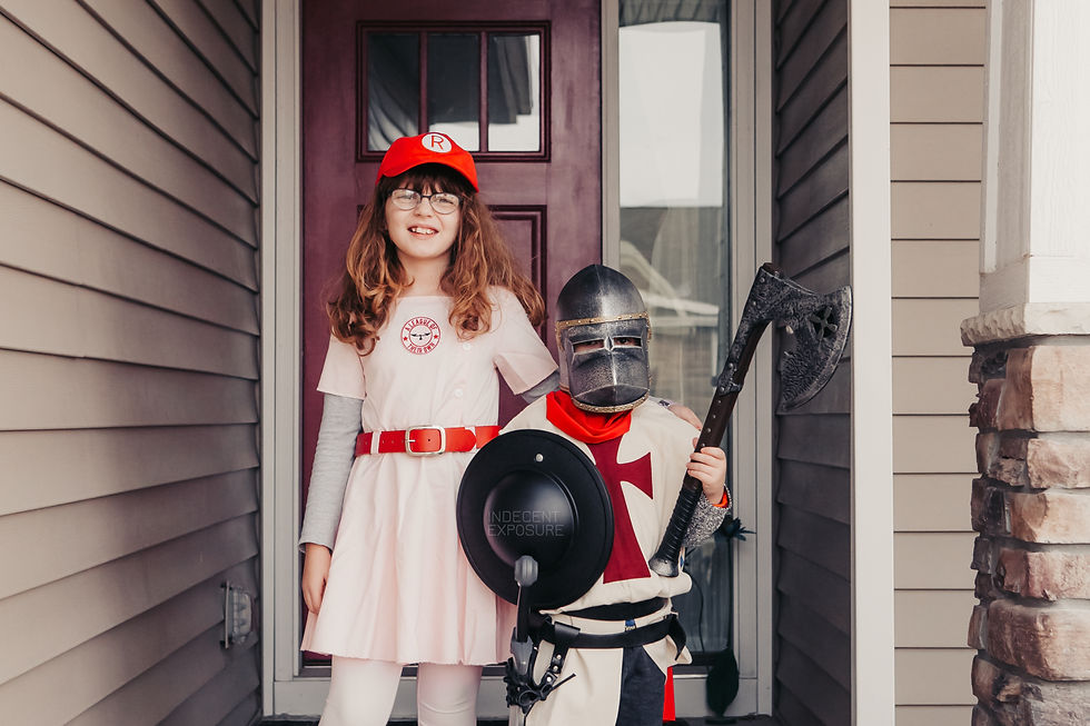 Two children in costumes stand on a porch. One wears a pink baseball uniform, the other a knight outfit with helmet and axe. Playful mood.