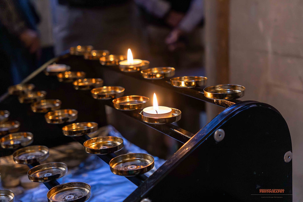 Candles lit in a dim setting on a black stand with gold holders, creating a serene atmosphere. Background is blurred with soft lighting.