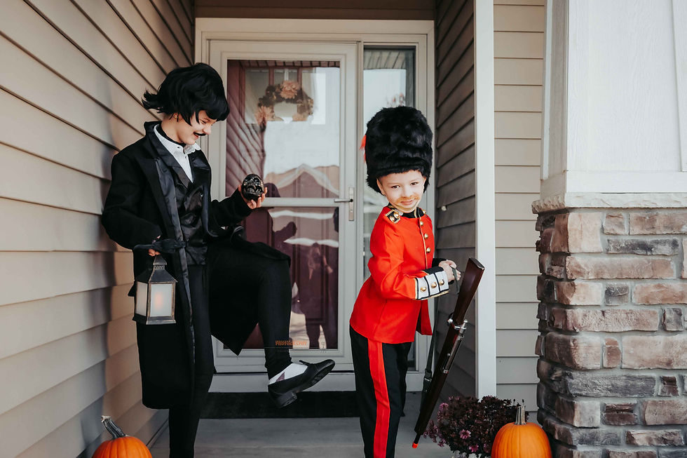 Two kids in costumes: one with a lantern and skull, the other in a red uniform, both on a porch with pumpkins, exuding playful joy.