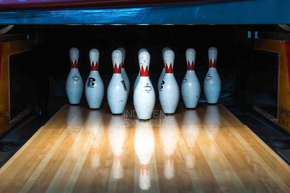 Seven bowling pins stand on a polished wooden lane with red and white stripes, creating a focused and anticipatory mood in the dim alley.