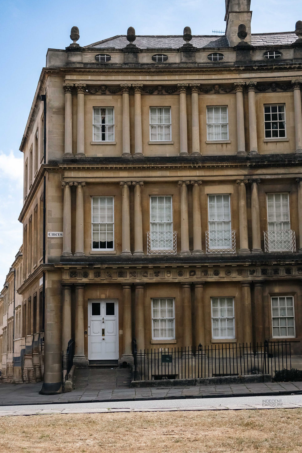 Classic stone building with columns, many windows, and a white door. "Circus" sign on the corner. Clear sky and sunny day.