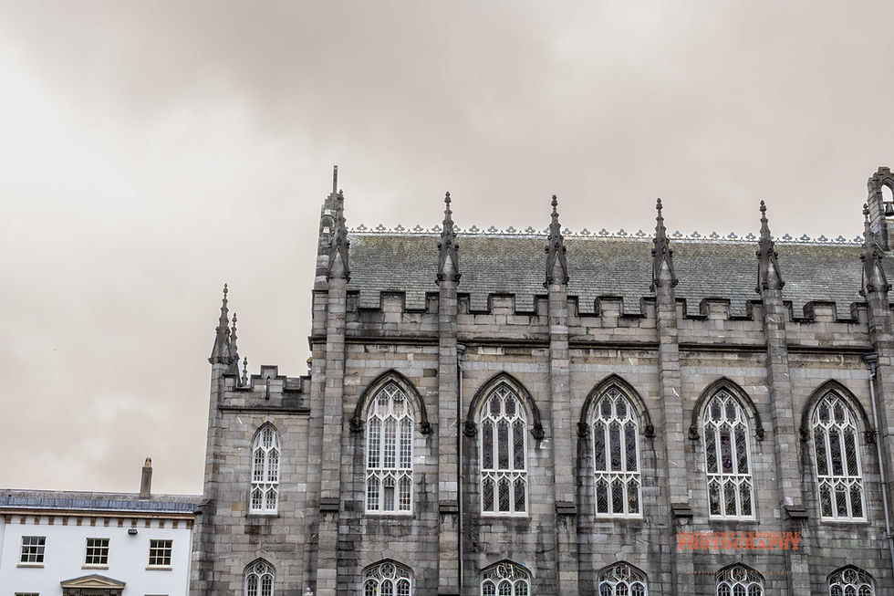 Gothic-style stone building facade with pointed arch windows, ornate spires, and cloudy sky. Text: Intrepid Exposure Photography.