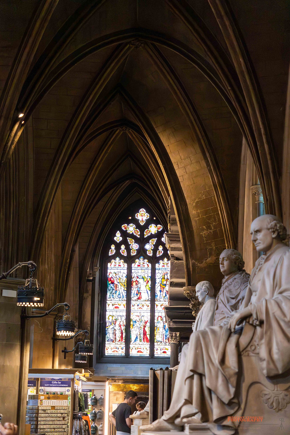 Gothic cathedral interior with statues, stained glass window, and gift shop. A person browses inside. Calm, historic atmosphere.