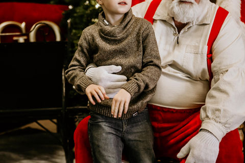 Santa holds a young boy by the stomach.