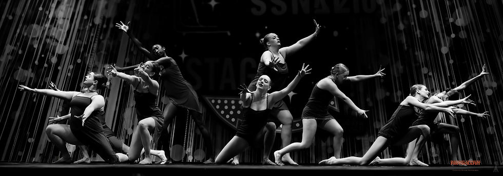 Dancers in black outfits pose dynamically on stage, arms extended, in dramatic black-and-white lighting. A backdrop with vertical lines.