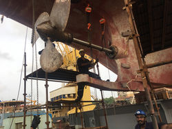Workers performing ship propeller and shaft maintenance at a dockyard.