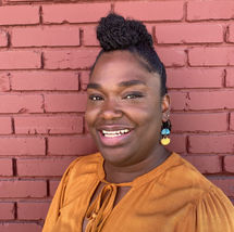 Black woman smiling in orange shirt in front of brick wall