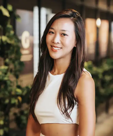 Cathy Lee smiling, in a white top with plants behind her