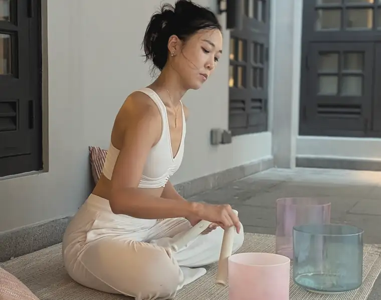 Cathy Lee seated on a woven mat with crystal singing bowls