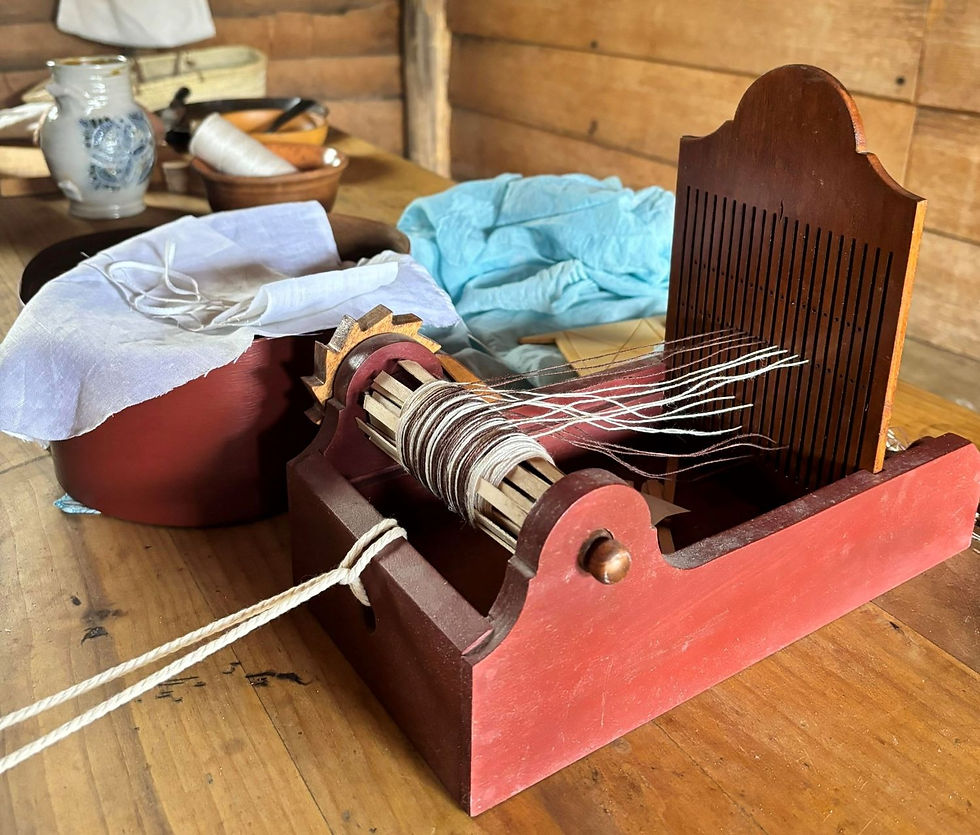 A tape loom with yarn threaded. In the background is baskets of fabric and string.