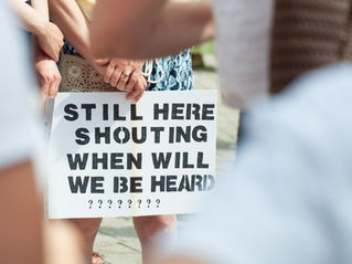 Sign that reads still here shouting when will we be heard