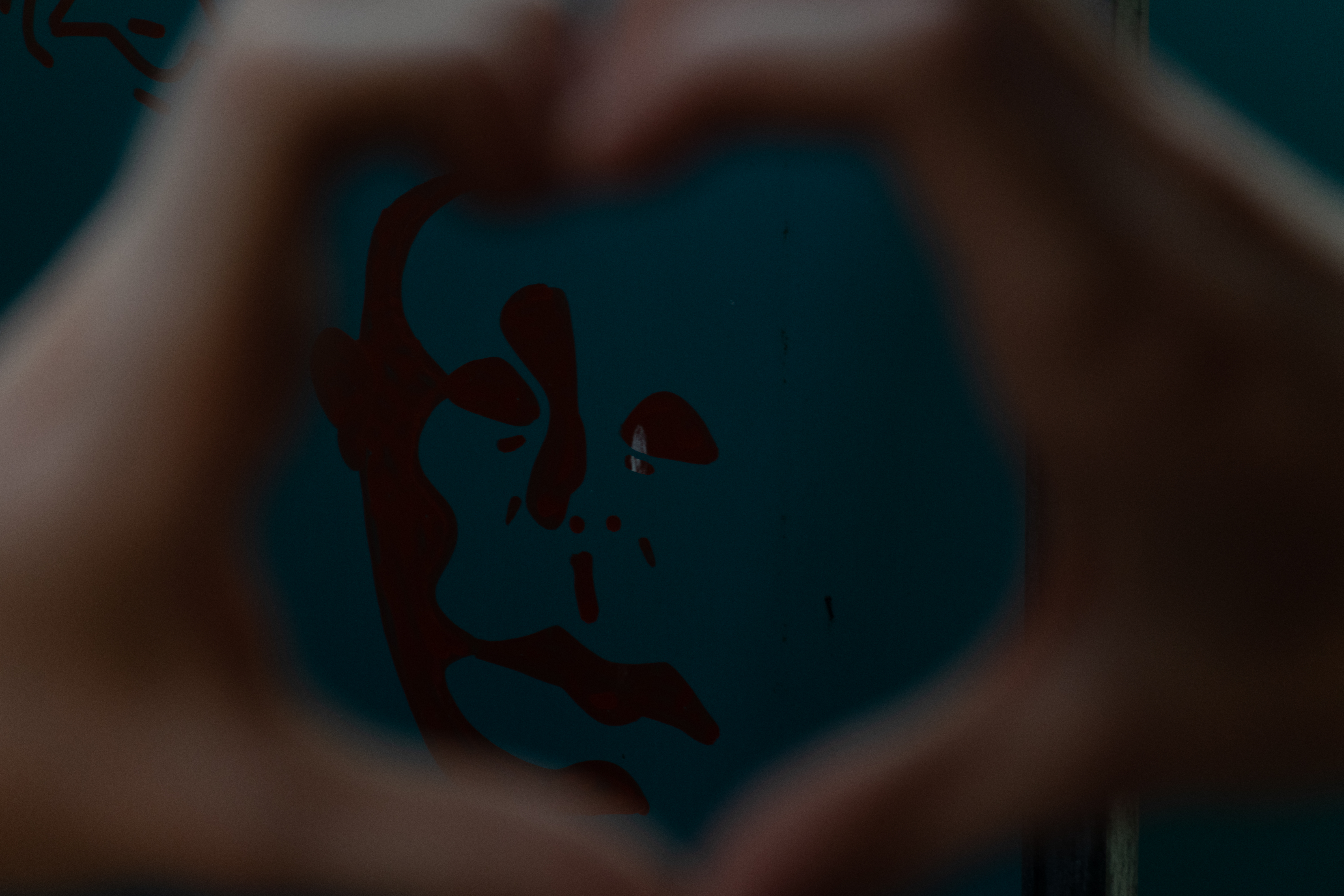 Bokeh effect on hands in foreground, spraypainted red scary face in background on a bathroom stall. 