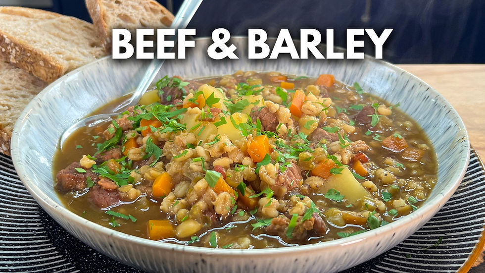 Bowl of beef and barley soup with carrots, herbs, and steam, surrounded by rustic bread. Text "BEEF & BARLEY" is visible above.