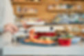 In the foreground, there is a plate of salmon garnished with lemon slices. On the left side of the image, a partially visible person is reaching for some salmon with a fork, holding another plate in their other hand. In the background, many other breakfast items like bread and more can be seen, suggesting a rich buffet spread.